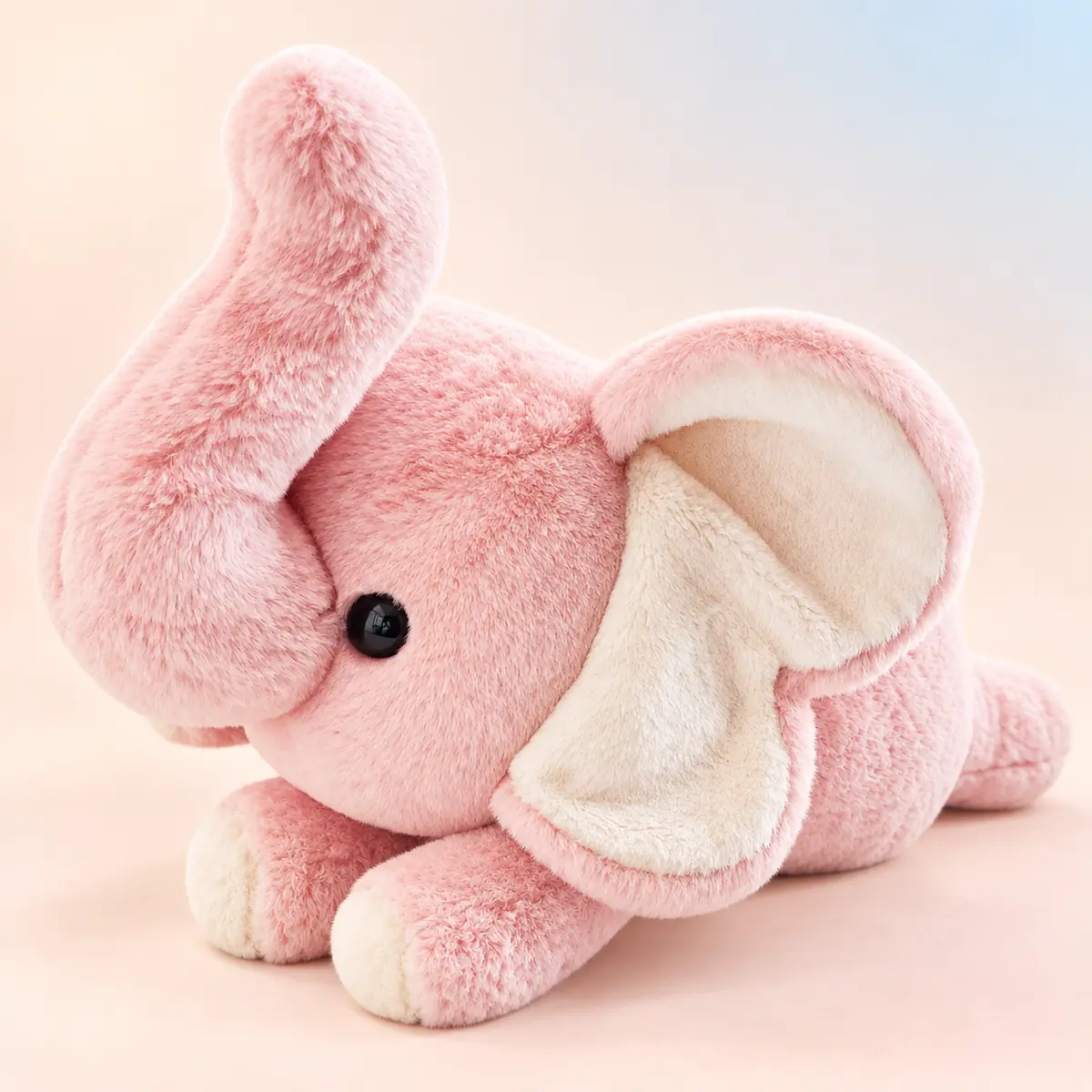 Poppy, the soft pink elephant weighted plush with a cream-lined ear and a curled trunk, lying down against a soft peach studio background