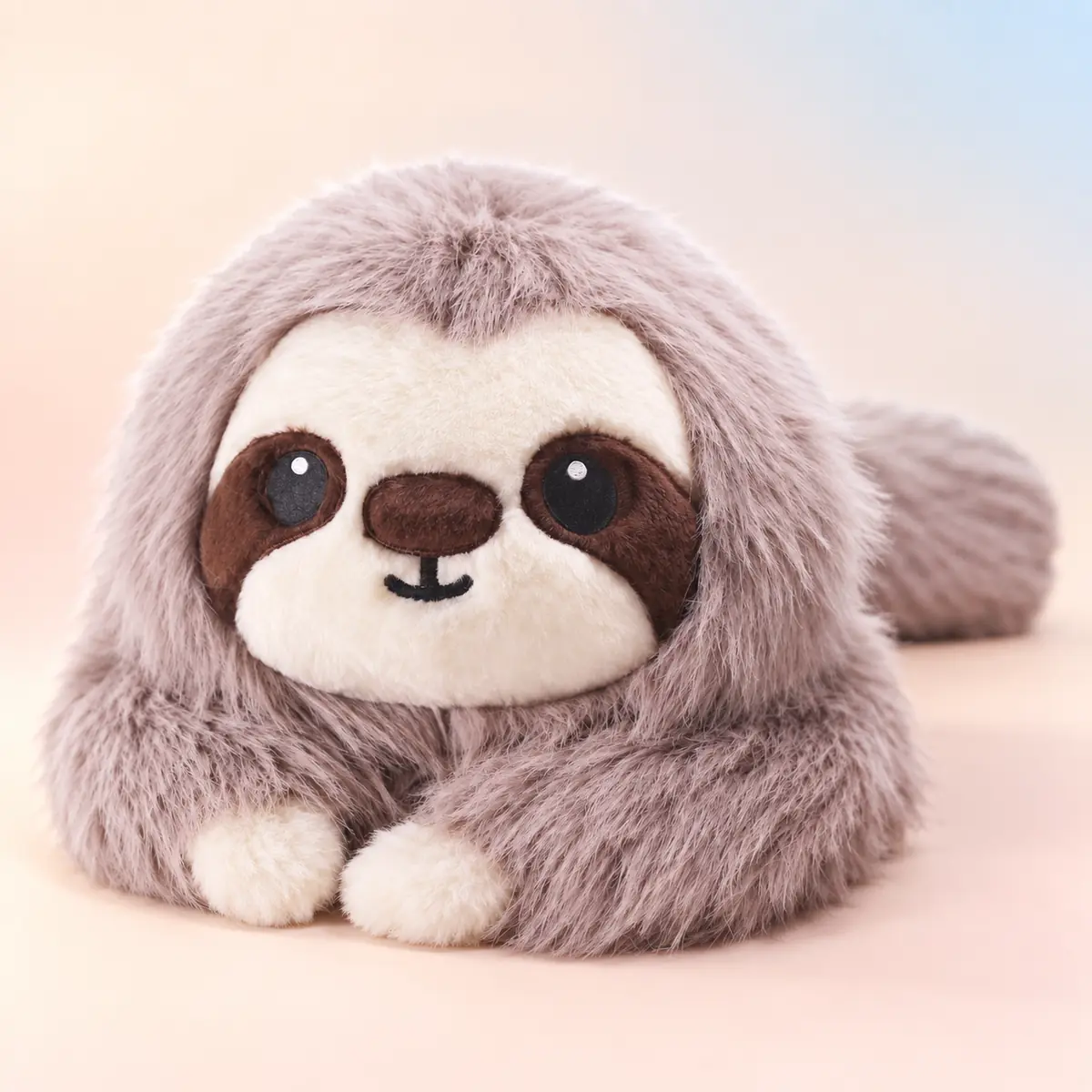 Moss, the grey sloth weighted plush with soft fluffy fur and dark eye patches, resting against a soft peach studio background